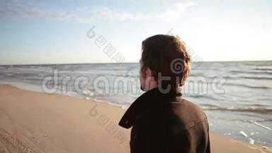 一个穿着黑色外套的年轻黑发男子的侧面景色正在沿着海岸散步。